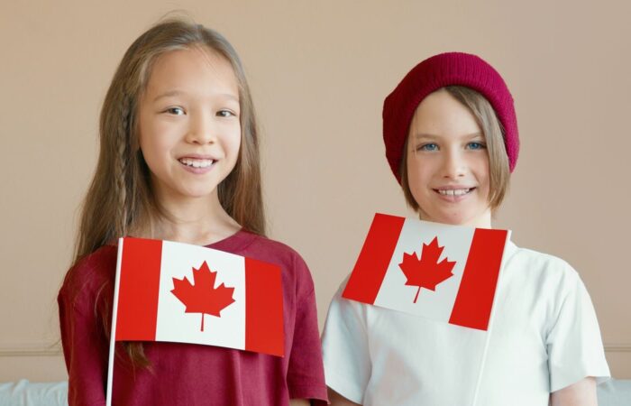 Two smiling children holding Canadian flags indoors, celebrating national pride.