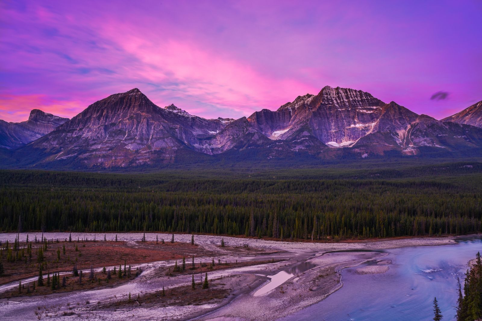 Breathtaking view of the Canadian Rockies at sunset with a vibrant purple sky.