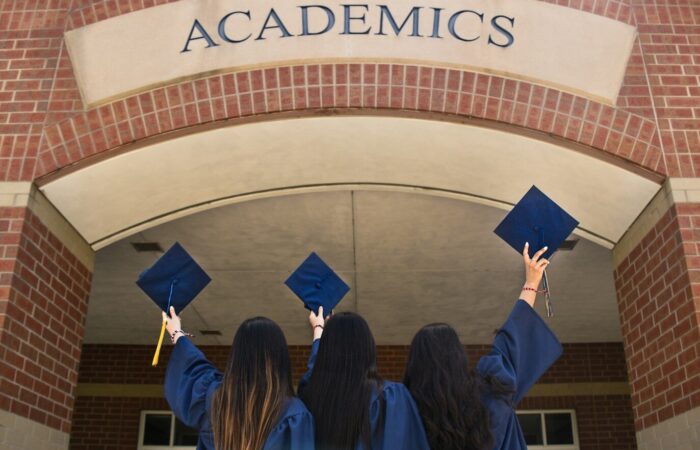 three girls in graduation gowns hold their caps in the air